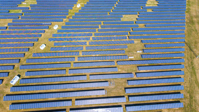 Aerial view of solar panels stretching across the landscape, reflecting the sky above, creating a mosaic of blue against the earth tones, Sevetin, South Bohemian Region, Czechia.