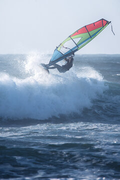 Cascais, Portugal - 28 March 2026: View of a windsurfer silhouetted against massive crashing waves at Praia do Guincho with white sea foam and deep blue water.