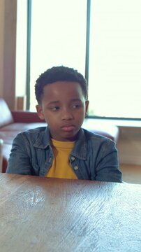 Vertical video: Plugging ears, boy crossing arms at table as hand reaching in living room in jacket