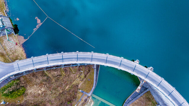 Aerial view of the Staudamm Klaus dam curving gracefully against the contrasting turquoise waters and the earthy landscape, Klaus an der Pyhrnbahn, Oberosterreich, Austria.