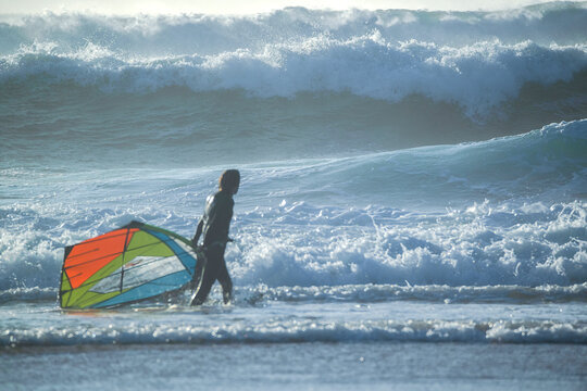 Cascais, Portugal - 28 March 2026: View of a windsurfer silhouetted against massive crashing waves at Praia do Guincho with white sea foam and deep blue water.