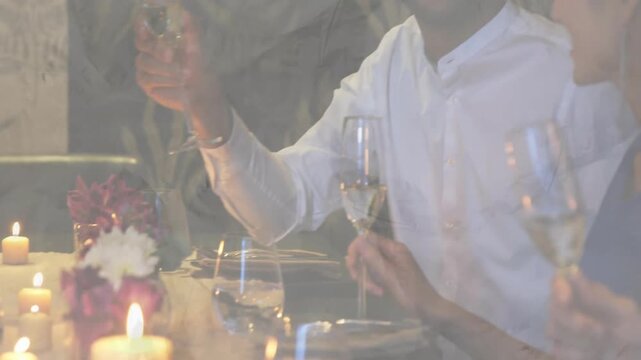 Vertical video: Smiling man in white shirt raising wine glass, friends toasting at candlelit table