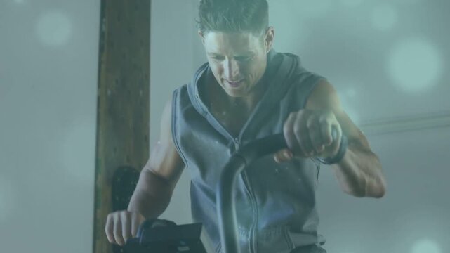 Leaning forward man gripping elliptical console in garage, wearing sleeveless hoodie and wristband