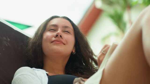 Happy tropical writer. Woman relaxing under sunlight while jotting notes on tropical island. Woman with cheerful expression writing in notebook surrounded by vibrant greenery on sunny island