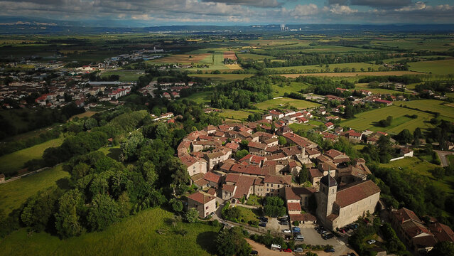 Aerial view of the medieval walled town basking in the sun, its ancient stones glowing warmly against the surrounding vibrant green fields, Perouges, Auvergne-Rhone-Alpes, France.
