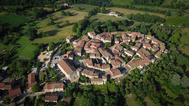 Aerial view of the ancient walled city with its reddish-brown rooftops contrasted against the surrounding vibrant green landscape, Perouges, Auvergne-Rhone-Alpes, France.