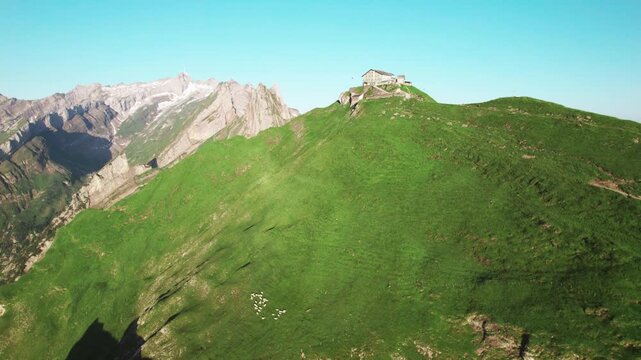 Aerial 4k drone view of Schaeffler Hut alpine mountain lodge atop a green ridge, Swiss Alps panorama, hiking destination, dramatic peaks, summer alpine landscape, travel tourism scenery