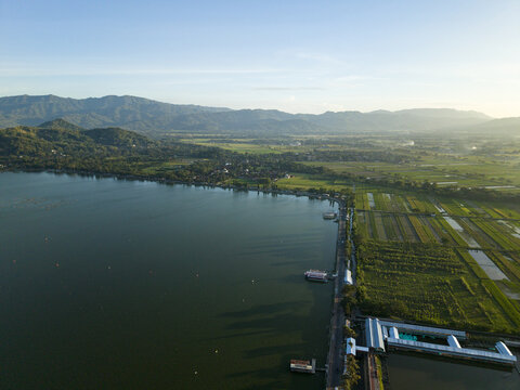Aerial view of the tranquil Rawa Jombor lake mirroring the sky, fringed by verdant rice paddies and distant mountains, Rawa Jombor Klaten, Klaten Regency, Jawa Tengah, Indonesia.