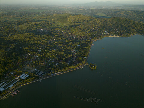 Aerial view of Rawa Jombor's tranquil waters meeting the lush green shoreline, creating a serene contrast of colors and textures, Klaten Regency, Jawa Tengah, Indonesia.