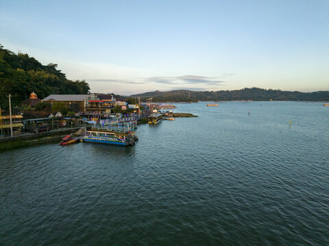 Aerial view of boats docked near buildings along the tranquil waters of Rawa Jombor under the soft glow of the setting sun, Klaten, Jawa Tengah, Indonesia.