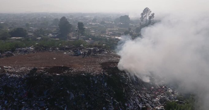 Aerial close-up fly over view. Burning rubbish causing greenhouse gas, contributor to climate change.  Extreme Poverty. People living alongside dumpsite struggling to survive through waste picking.