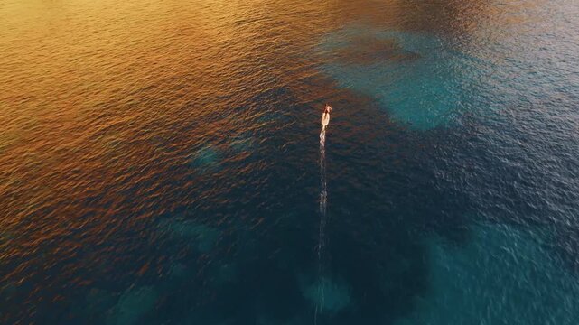 Aerial view of motor boat and jet ski cruising on crystal clear turquoise water during golden sunset