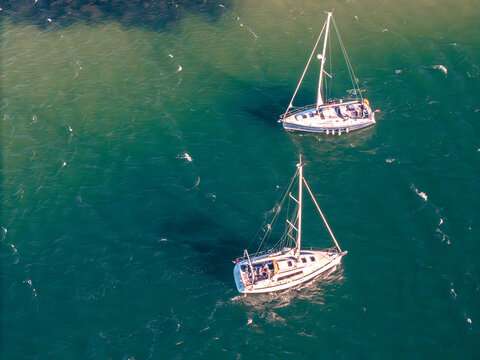 Aerial view of two sailboats sailing on the turquoise waters of the Atlantic Ocean with people on deck in Cascais, Portugal.