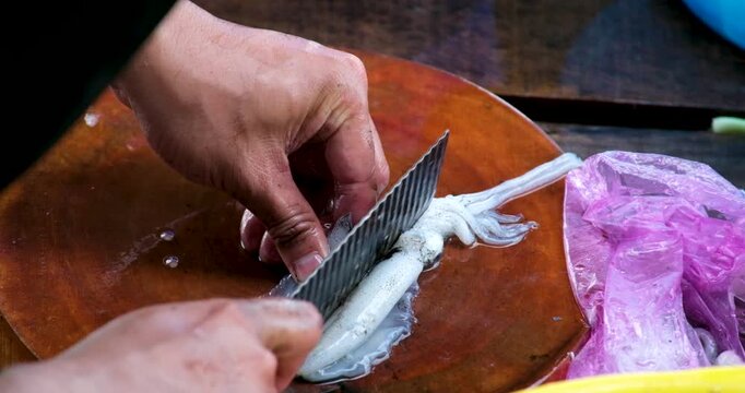 Squid cleaning and preparation by hand with ink release washing in blue basin and draining in yellow colander showing traditional Asian seafood process