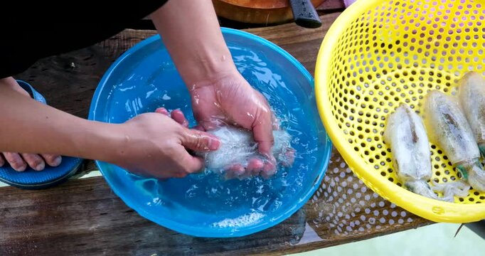 Squid cleaning and preparation by hand with ink release washing in blue basin and draining in yellow colander showing traditional Asian seafood process
