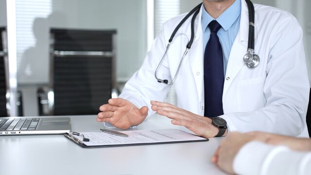 Male doctor communicating with patient at a clinic desk, offering professional healthcare guidance and explaining a diagnosis. Medicine, healthcare and science concept