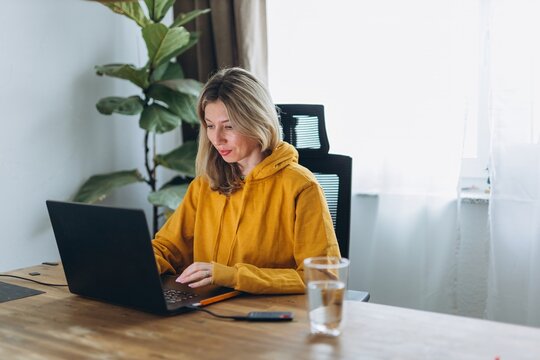 Woman working on laptop in minimal home office showing digital minimalism and focused solitude in quiet intentional work environment