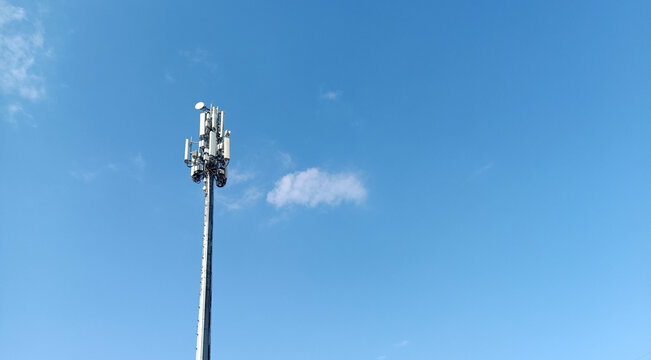 A modern telecommunication cell tower (BTS) with antennas and transmitters against a clear blue sky. Concept of 5G, mobile network, signal coverage, and wireless technology