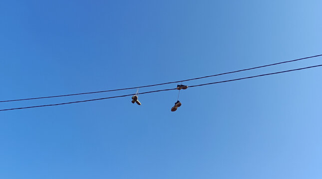 Urban Shoefiti Featuring Sneakers Hanging from an Overhead Power Line Against a Clear Blue Sky