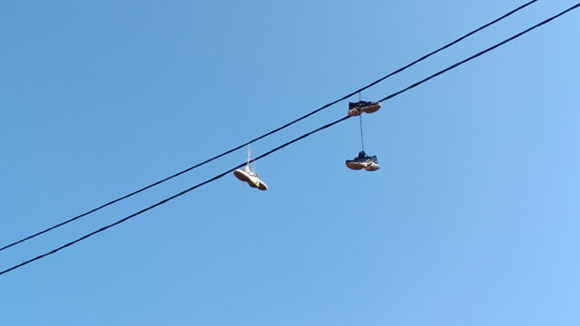 Urban Shoefiti Featuring Sneakers Hanging from an Overhead Power Line Against a Clear Blue Sky