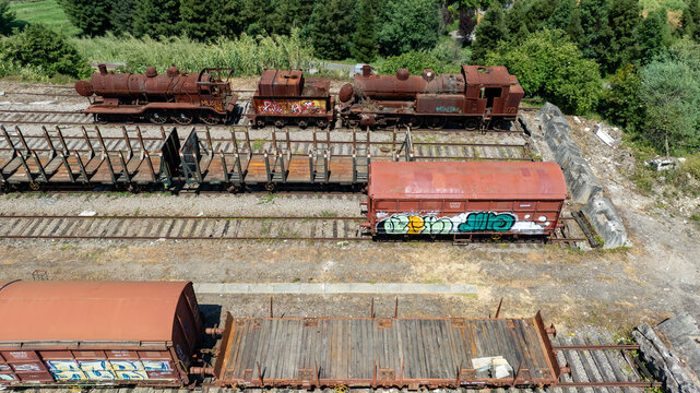 Aerial view of decaying trains and wagons rest on aged tracks, their rusted surfaces contrasting with the surrounding greenery, Vila Nova de Gaia, Porto District, Portugal.