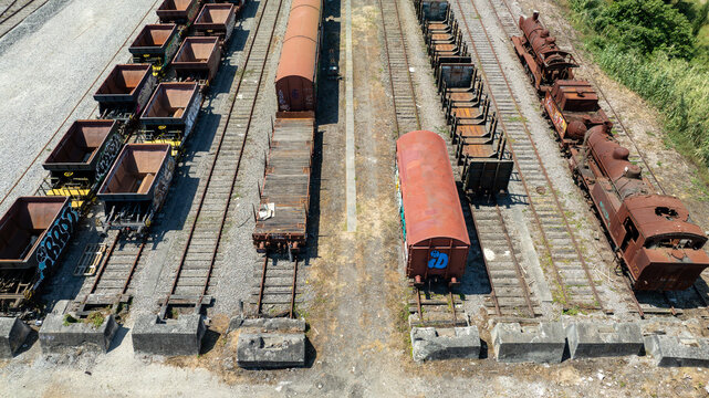 Aerial view of weathered trains and railcars stand still on parallel tracks, their rusty exteriors contrasting with the surrounding gravel and vegetation, Vila Nova de Gaia, Portugal.