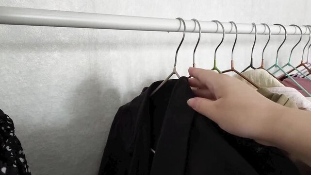 female hand selecting a clothe from a wardrobe full of clothes on hangers. Concept of clothing choice, daily routine and personal style.