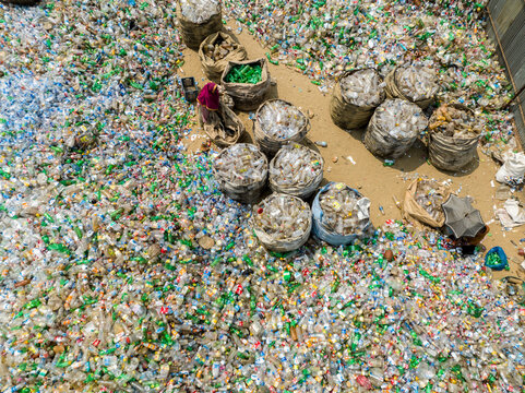 Aerial view of a sea of discarded bottles and plastic waste, contrasting with the orderly rows of filled jute bags, Chattogram, Bangladesh.