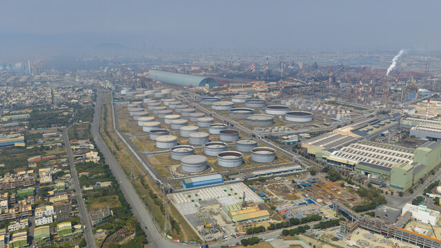 Aerial view of a vast industrial landscape with a cluster of circular storage tanks gleaming under the sunlight, amidst a network of roads and buildings, Kaohsiung City, Taiwan.