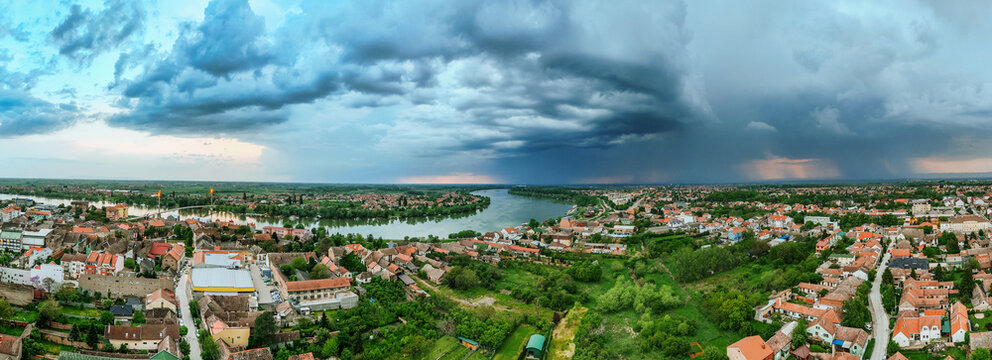 Aerial view of a serene river bisecting the landscape under a dramatic sky, casting shadows over the rooftops of the town, Sremska Mitrovica, Vojvodina, Serbia.