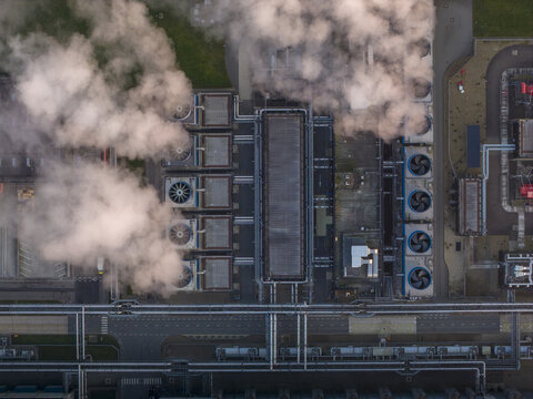 Aerial view of industrial facility with large cooling towers generating steam. Complex network of pipes, buildings, and infrastructure