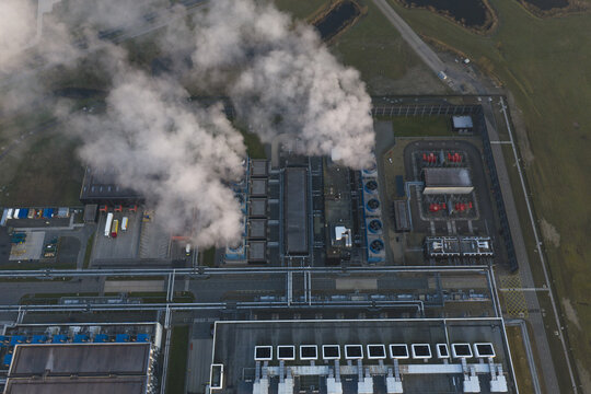 Aerial view of an industrial power plant or factory with multiple cooling towers releasing large plumes of steam into the sky