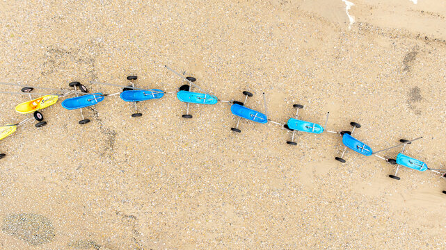 Aerial view of vibrant blue and yellow land yachts lined up like jewels on the sandy shore, Fort-Mahon-Plage, Hauts-de-France, France.