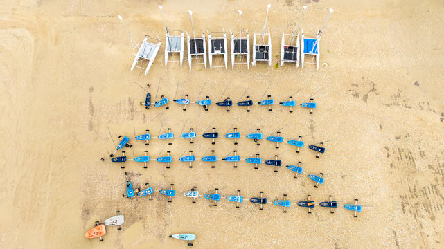 Aerial view of catamarans and windsurfing boards lined up on the sandy beach, a geometric tapestry of blue and white against the golden shore, Fort-Mahon-Plage, Hauts-de-France, France.