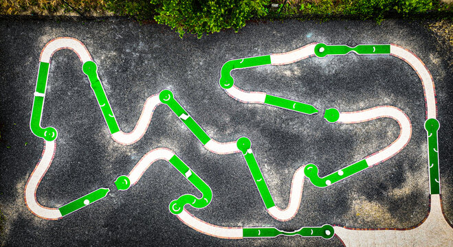 Aerial view of a winding pump track, its green and white stripes contrasting against the dark asphalt, creating a playful pattern from above, Fort-Mahon-Plage, Hauts-de-France, France.