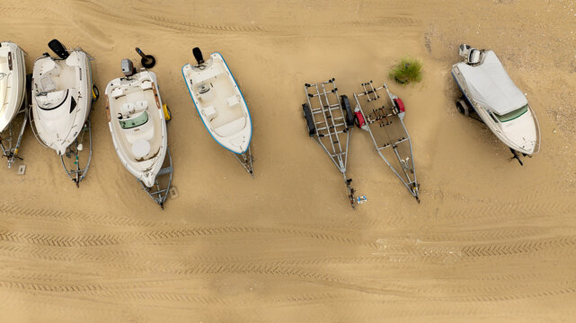 Aerial view of various boats resting on the sandy beach, their forms creating a geometric tableau against the textured ground, Fort-Mahon-Plage, Hauts-de-France, France.