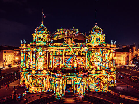 Aerial view of a theatre facade illuminated with vibrant colors and intricate patterns, creating a mesmerizing spectacle at night, Zagreb, Croatia.