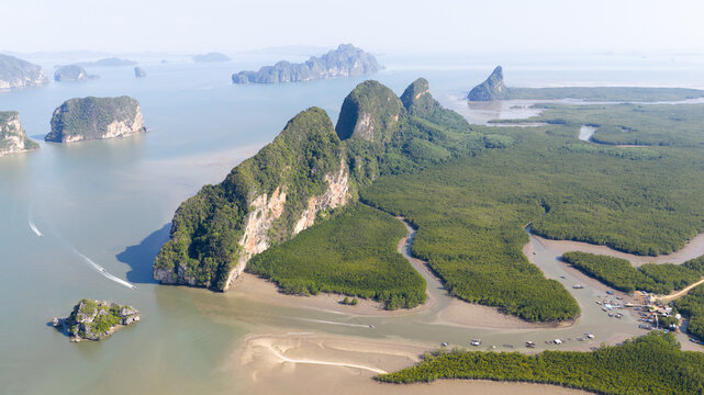 Aerial view of limestone karsts rising from the sea and lush mangrove forests along a winding river with small boats Phang Nga, Thailand.