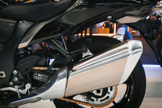 Rear motorcycle assembly with metallic exhaust, swingarm, chain drive, and wheel fitted with a sporty profile tire.