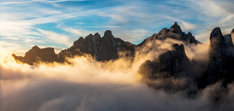 Aerial view of jagged peaks in Badia valley pierce through a sea of swirling mist under a sky streaked with dawn's light, Trentino-Alto Adige, Italy.