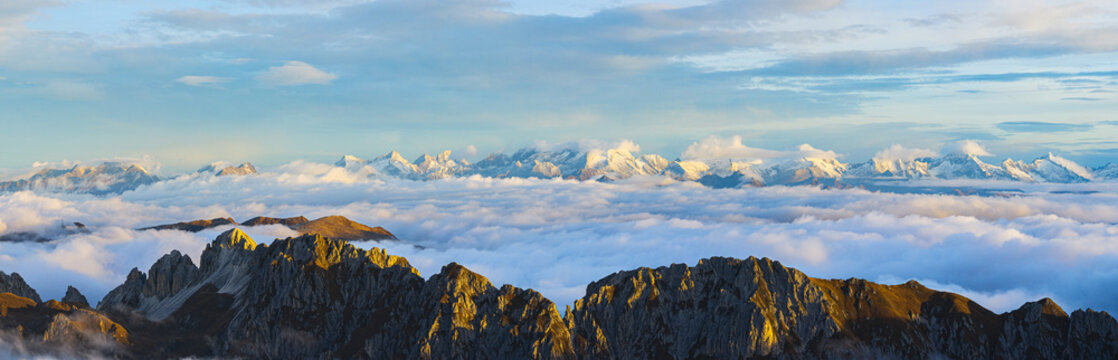 Aerial view of jagged peaks emerge from a sea of clouds, kissed by the golden light of dawn, contrasting with the distant snow-capped mountains, Trentino-Alto Adige, Italy.
