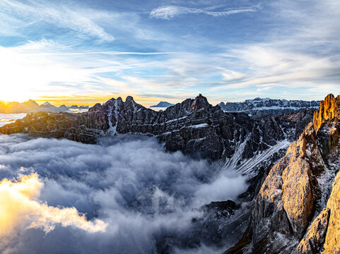 Aerial view of jagged peaks pierce through a sea of clouds, the sun painting the sky with hues of gold and the dramatic Dolomites rise majestically, Odle-Geisler, Trentino-Alto Adige, Italy.