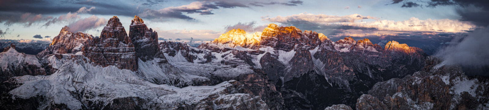 Aerial view of Tre Cime di Lavaredo and Croda dei Torni crowned with snow at sunset, contrasting with the dark shadows below, Dolomites, Italy.