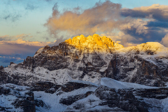 Aerial view of the Dolomites' Cima Undici and Cresta Zsigmondy kissed by the sun's golden light, a majestic dance of shadow and snow, Cortina d'Ampezzo, Veneto, Italy.