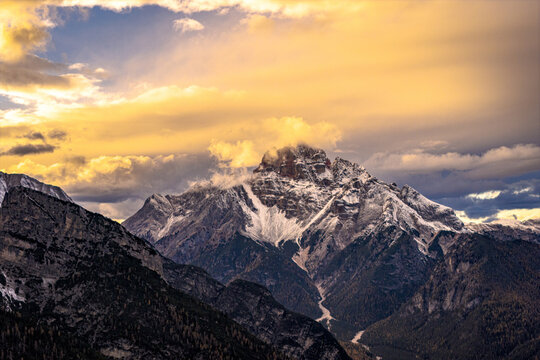 Aerial view of Croda Rossa peaks piercing through a golden sky, dusted with snow and shadowed by dramatic clouds, Cortina d'Ampezzo, Veneto, Italy.