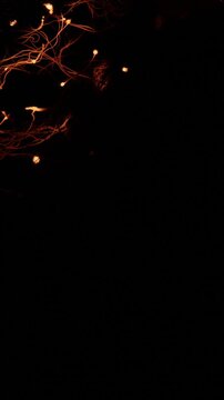 Hot glowing embers from burning steel wool floating and spinning against a dark background, creating fiery trails of light and smoke in a spectacular combustion and oxidation reaction