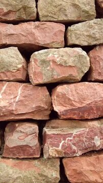 Close-up of a rustic dry-stone wall made of stacked red sandstone blocks. Natural building material background with rough texture