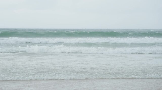 Overcast ocean waves roll toward shore, soft breakers and muted teal water under cloudy sky frame evokes coastal surveyor scanning swell, frame suggests beachcomber collecting drift, frame imagines
