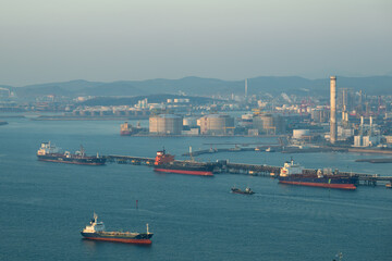 Naklejka premium Oil tankers unloading at an oil refinery in Ulsan. Aerial view of port oil infrastructure, storage terminal pier and refinery plants.