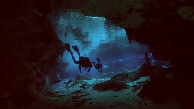 Underwater diver crosses illuminated cave chamber with strong light rays entering from opening in Cenote Dos Ojos, Quintana Roo, Mexico
